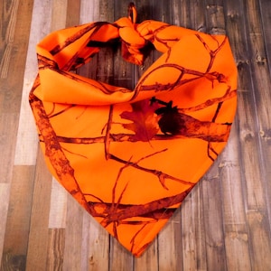 May include: Orange and brown camouflage bandana with a knotted design. The bandana is made of a soft, comfortable fabric and is perfect for adding a touch of style to any outfit.