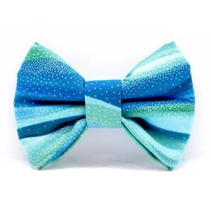 May include: A blue and green bow tie with a white speckled pattern. The bow tie is made of fabric and has a classic bow shape.