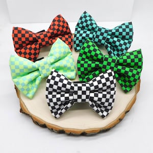 May include: A collection of six bow ties with a checkered pattern in various colors: red and black, teal and black, green and black, light green and blue, and black and white. The bow ties are arranged on a wooden slice.