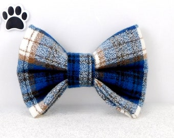 May include: A blue plaid bow tie with white and brown accents. The bow tie is made of a soft, textured fabric. The bow tie is a pet accessory.