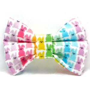 May include: A rainbow-colored bow tie with a pattern of pastel bunny rabbits. The bow tie is made of fabric and has a white background.