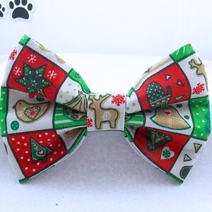 Puede incluir: Una pajarita festiva con un diseño de patchwork con ilustraciones navideñas. La pajarita muestra cuadrados rojos, verdes y blancos con imágenes de renos, pájaros y árboles de Navidad. Un accesorio perfecto para mascotas.