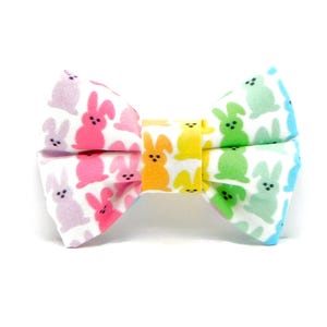 May include: A rainbow-coloured bow tie with a pattern of pastel-coloured bunnies. The bow tie is made of fabric and has a white background.