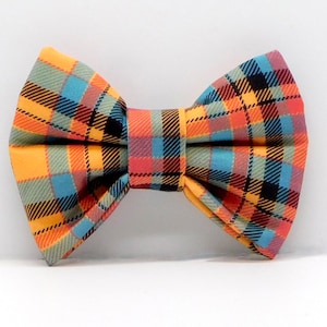 May include: A colourful bow tie featuring a plaid pattern in yellow, orange, blue, and black. The bow tie is pre-tied with a symmetrical shape. The fabric has a woven texture, and the design is a classic tartan pattern.