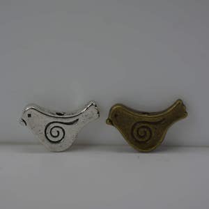 May include: Two metal bird charms, one silver and one bronze, with a swirl design.