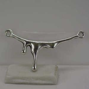 May include: Silver pendant with a dripping design. The pendant is shaped like a curved line with a series of drops hanging from it.