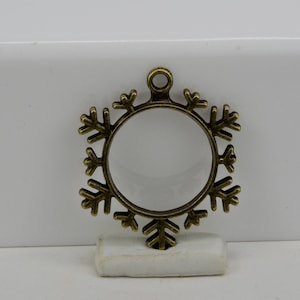 May include: A gold-toned metal snowflake charm with a circular opening in the center. The charm has a loop at the top for hanging.