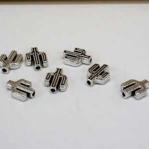 May include: Eight silver cactus-shaped beads with black outlines. The beads are small and have a hole in the center for stringing.