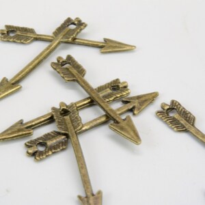 May include: A group of six antique gold arrow charms. The arrows are made of metal and have a detailed design. They are perfect for adding a touch of rustic charm to your jewelry or crafts.