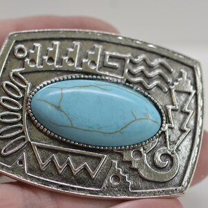 May include: Silver pendant with a turquoise stone set in a geometric design. The pendant has a loop for attaching a chain.