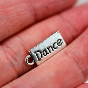 Peut inclure: Breloque en argent avec le mot "Dance" gravé dessus. Le breloque a une boucle pour l'attacher à un bracelet ou un collier.