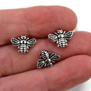 May include: Three silver bee charms with detailed wings and bodies. The bees are about 1/2 inch in size.