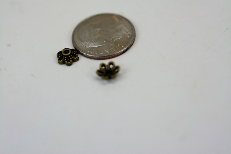 May include: Two small, gold-colored metal flower-shaped bead caps, next to a US dime for size comparison.