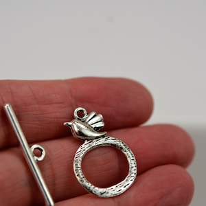 May include: Silver tone metal toggle clasp with a bird design. The clasp has a round ring and a straight bar.