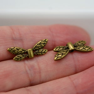 May include: Two gold-toned metal butterfly charms with a leaf design. The charms have a hole in the center for attaching to jewelry or other crafts.