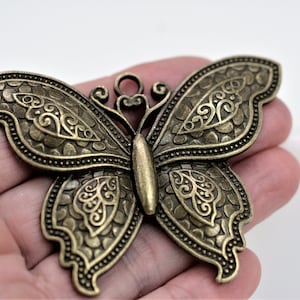 May include: A detailed, bronze-coloured butterfly pendant with intricate patterns on its wings. The butterfly has a textured surface and a loop at the top for hanging. The wings are adorned with ornate, swirling designs.