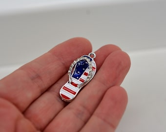 May include: A silver charm in the shape of a flip-flop with red, white, and blue enamel and rhinestones.