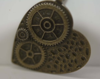 May include: A heart-shaped pendant with a steampunk design featuring three intricate gears. The gears are made of metal and have a bronze finish. The pendant is attached to a chain.