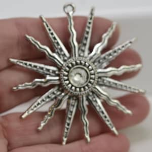 May include: Silver-toned starburst pendant with a clear rhinestone in the centre. The pendant has a textured, ornate design.