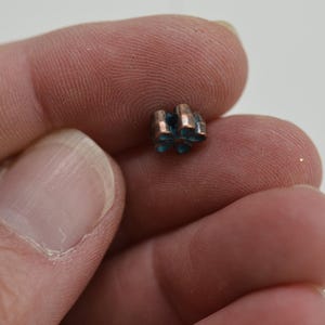 May include: A small, copper-colored charm with a blue, star-shaped design. The charm is held in a person's hand.