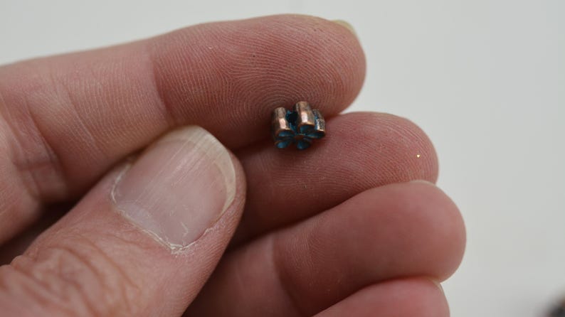 May include: A small, copper-colored charm with a blue, star-shaped design. The charm is held in a person's hand.