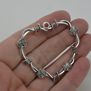 May include: Silver-toned heart-shaped pendant with a barbed wire design and rose accents.