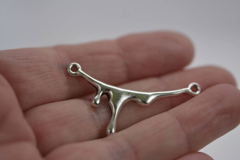 Puede incluir: Encanto de metal plateado con forma de l&iacute;quido que gotea, con dos bucles para sujetarlo a joyas u otras manualidades.