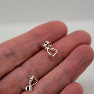 May include: Two silver-toned pendant clasps, one in a traditional horseshoe shape and the other in a more modern, rounded design. Both clasps are designed for attaching to necklaces or bracelets.