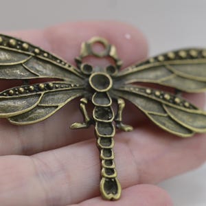 May include: A bronze dragonfly charm with detailed wings and a beaded body. The charm has a loop at the top for attaching to jewellery or other crafts.