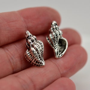 May include: Two silver-toned seashell charms. The charms are detailed and have a realistic look.