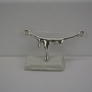 Puede incluir: Pendiente de plata con un dise&ntilde;o de goteo. El pendiente tiene forma de l&iacute;nea curva con una serie de gotas que cuelgan de &eacute;l.