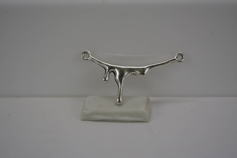 Puede incluir: Pendiente de plata con un dise&ntilde;o de goteo. El pendiente tiene forma de l&iacute;nea curva con una serie de gotas que cuelgan de &eacute;l.