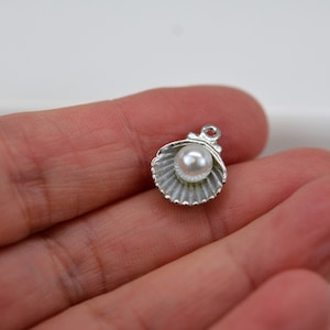 May include: Silver charm featuring a seashell with a white pearl inside. The charm has a loop for attaching to a necklace or bracelet.
