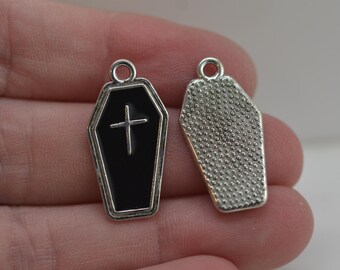 May include: Two coffin-shaped charms. One charm is black with a silver cross and silver trim. The other charm is silver with a textured pattern. Both charms have a loop at the top for attaching to jewelry.