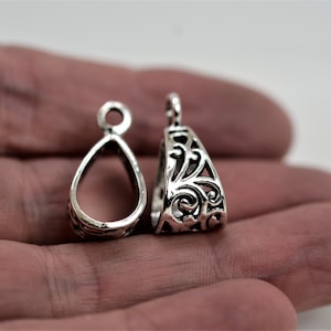 May include: Two silver pendant bails with an ornate design. One bail is open and the other is closed.