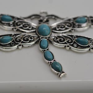 May include: Silver dragonfly pendant with turquoise blue stones. The dragonfly has intricate filigree details and a long, slender body.