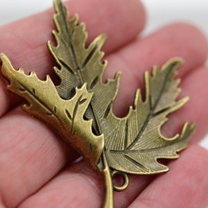 May include: Two antique gold-toned metal leaves with detailed etching. The leaves are connected by a loop at the bottom.