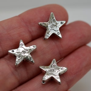 May include: Three silver star-shaped charms with a swirl design. The charms are about 1 inch in size.