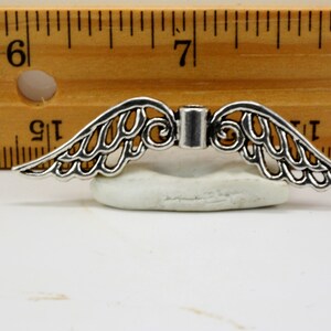 May include: Silver filigree angel wings charm with a decorative center piece. The wings are approximately 1 1/2 inches wide.