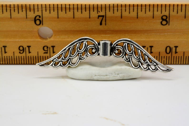 May include: Silver filigree angel wings charm with a decorative center piece. The wings are approximately 1 1/2 inches wide.