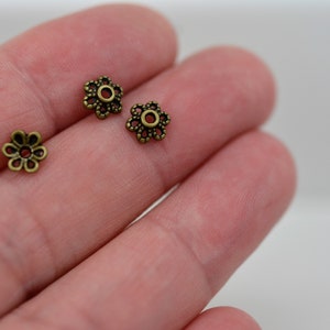 May include: Three antique gold-toned metal flower-shaped bead caps with a small hole in the center.