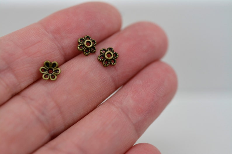 May include: Three antique gold-toned metal flower-shaped bead caps with a small hole in the center.