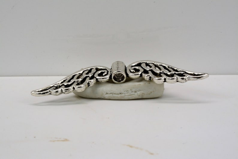 May include: Silver angel wing charm with a clear crystal in the center. The charm is designed to be used as a pendant or a bead for jewelry making.