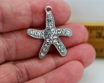 Op de afbeelding: Zilveren zeester charm met heldere strass steentjes. De charm is ongeveer 5 cm breed en perfect voor het maken van sieraden.