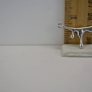 Puede incluir: Encanto de metal plateado en forma de l&iacute;quido que gotea con dos anillos de salto. El encanto mide aproximadamente 2,5 cm de largo y se mide contra una regla.