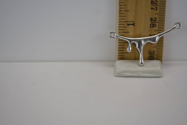 Puede incluir: Encanto de metal plateado en forma de l&iacute;quido que gotea con dos anillos de salto. El encanto mide aproximadamente 2,5 cm de largo y se mide contra una regla.