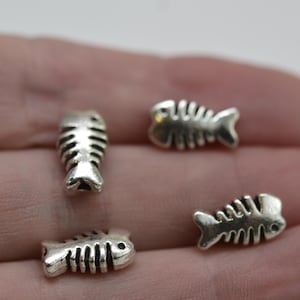 May include: Four small, silver-colored fish bone charms. The charms are detailed with rib-like lines and a small eye. These charms are ideal for jewelry making or other craft projects.