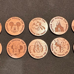 May include: Ten round wooden tokens with different Disney characters and the text "Thanks for making the magic!"  Each token features a different character, including Mickey Mouse, Minnie Mouse, Donald Duck, Goofy, and Cinderella.
