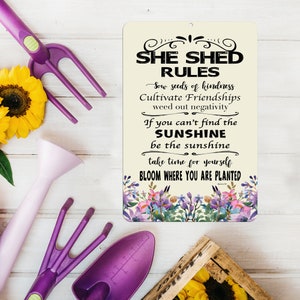 May include: A cream-colored sign with black text that reads "She Shed Rules" and includes a floral design. The text reads "Sow seeds of kindness, Cultivate Friendships, weed out negativity. If you can't find the sunshine, be the sunshine. Take time for yourself. Bloom where you are planted."
