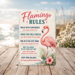 May include: A rectangular metal sign with a distressed finish features a pink flamingo illustration and the words "Flamingo Rules." The sign includes inspirational quotes about confidence, joy, and balance, with a tropical beach scene in the background.